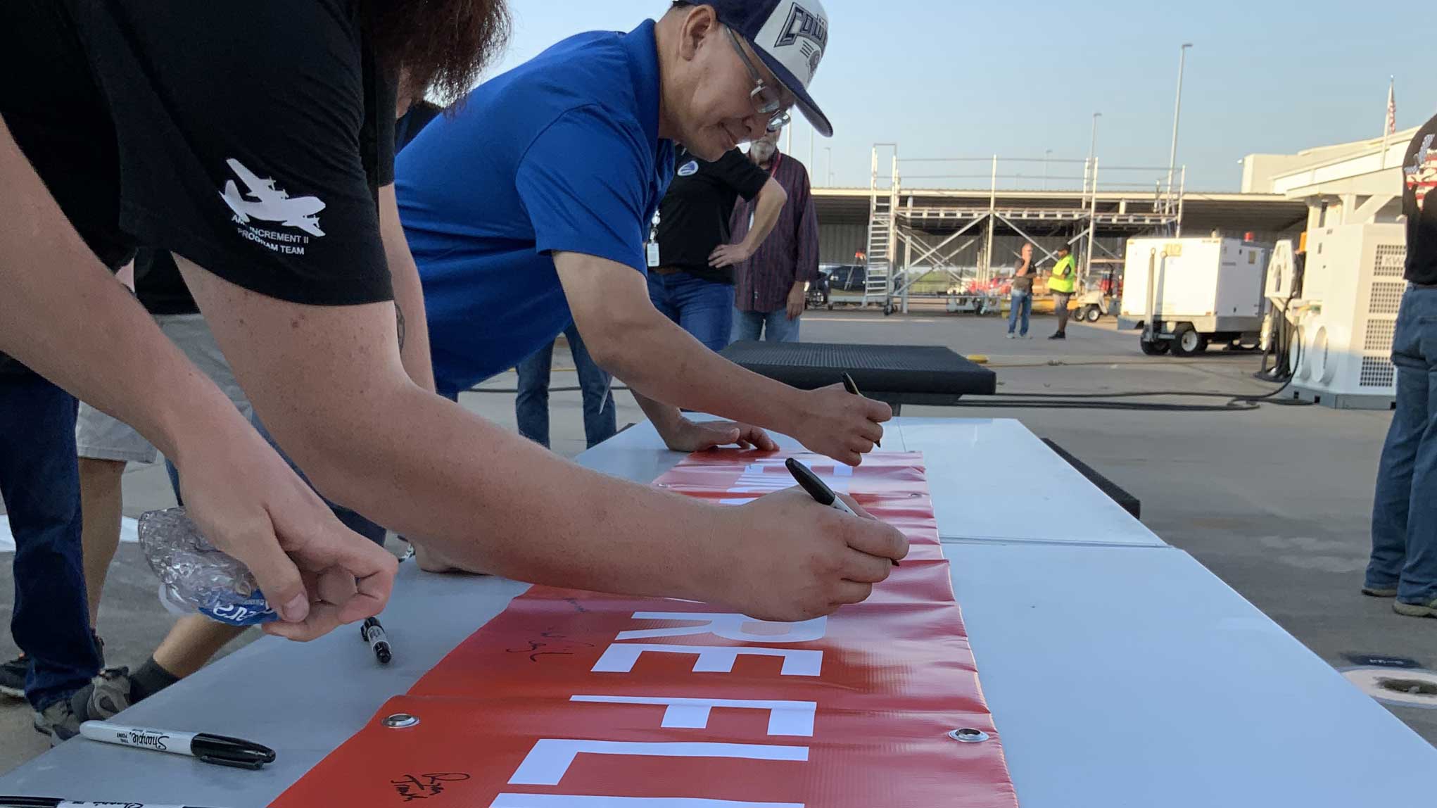 L3Harris team members sign a banner celebrating the AMP INC 2 milestone