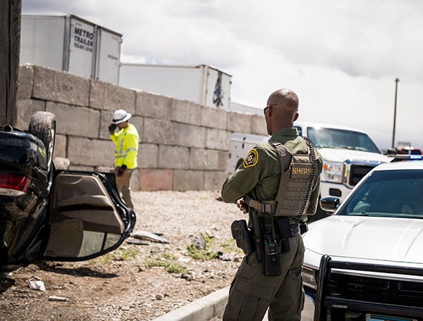 Law enforcement officer with XL series radio near vehicle wreckage 