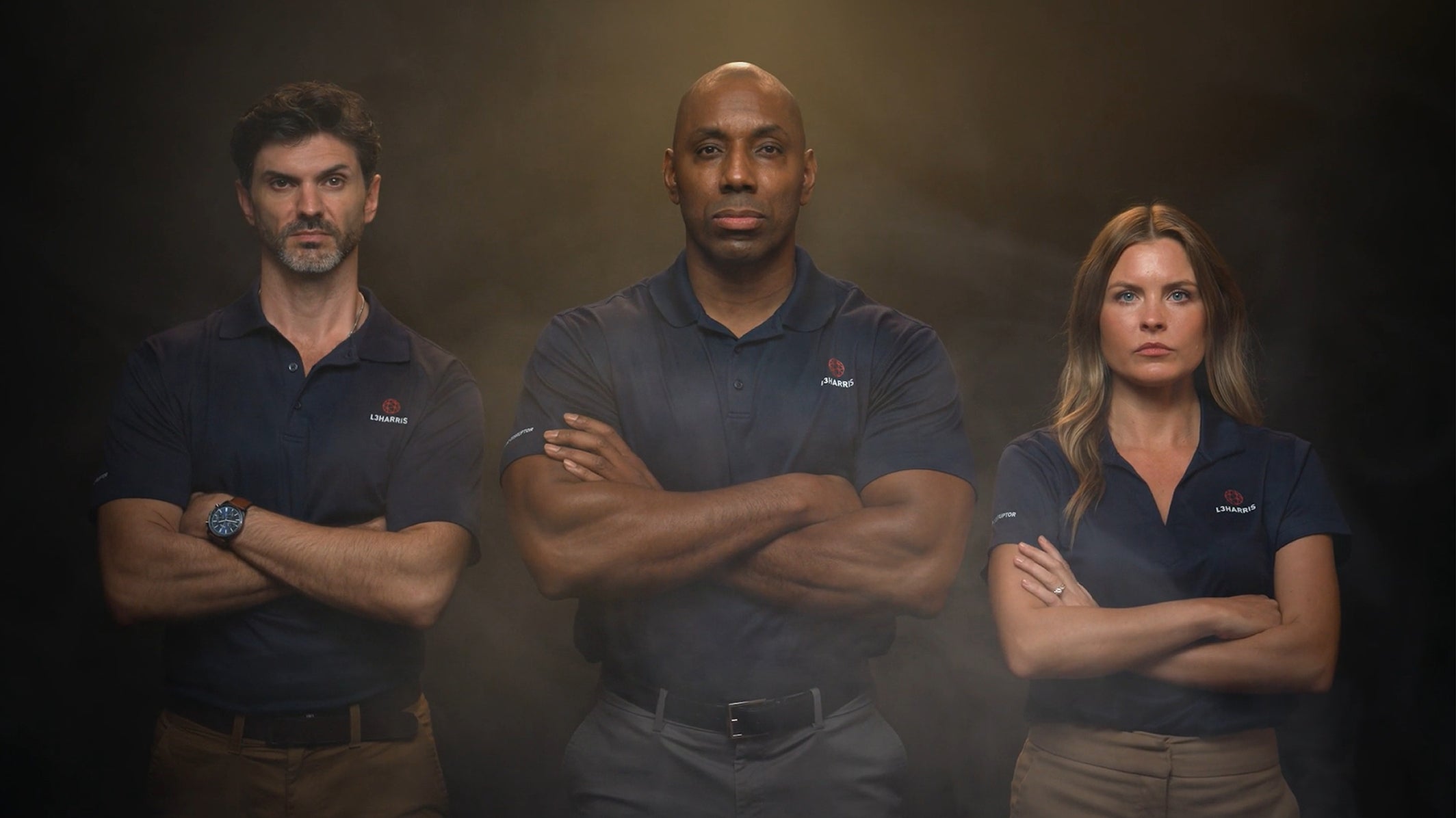Three L3Harris employees stand with arms crossed
