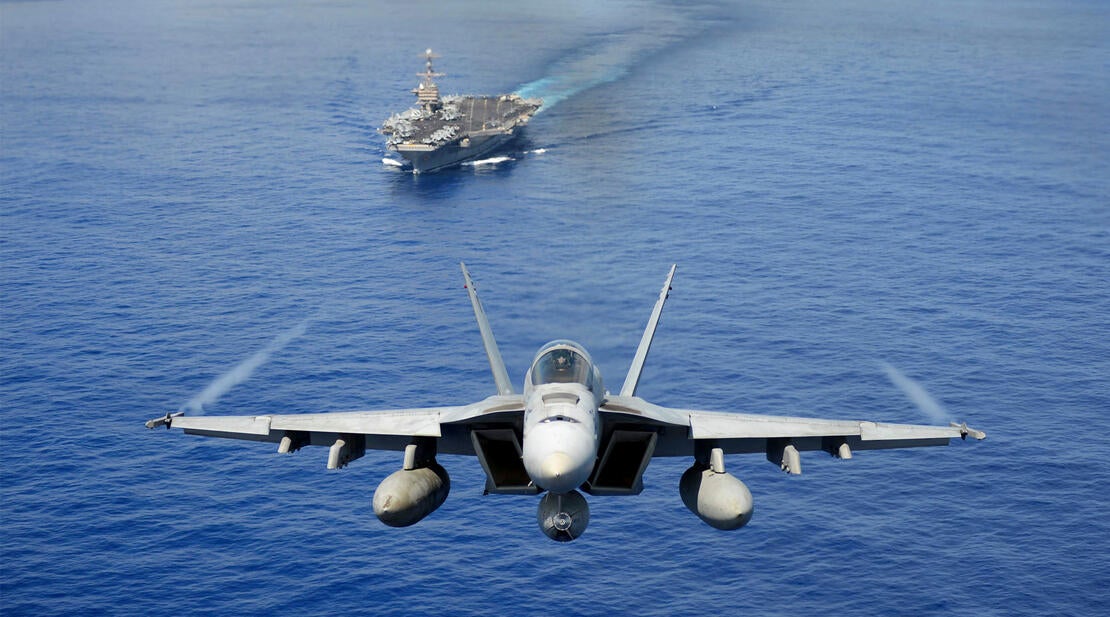 A jet flies over a ship at sea