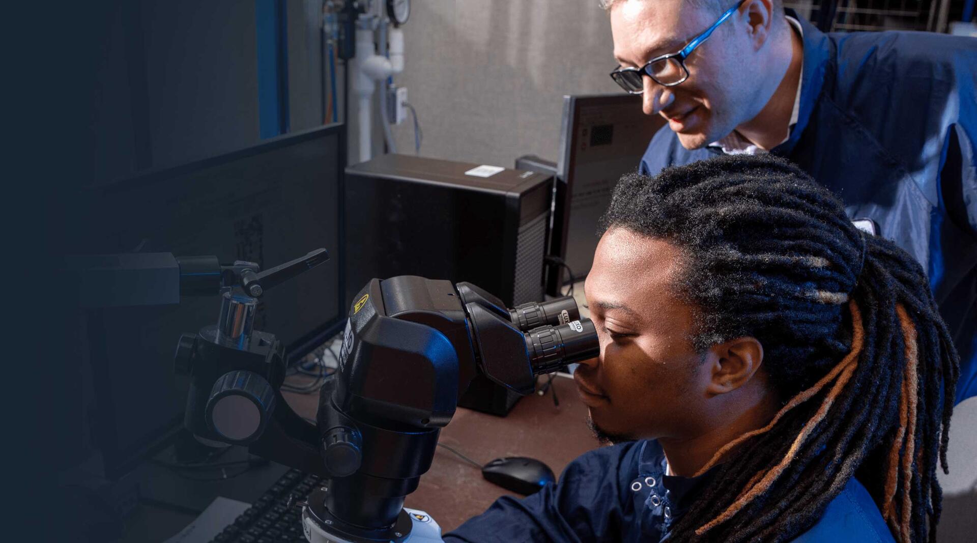 Two male employees looking through microscope