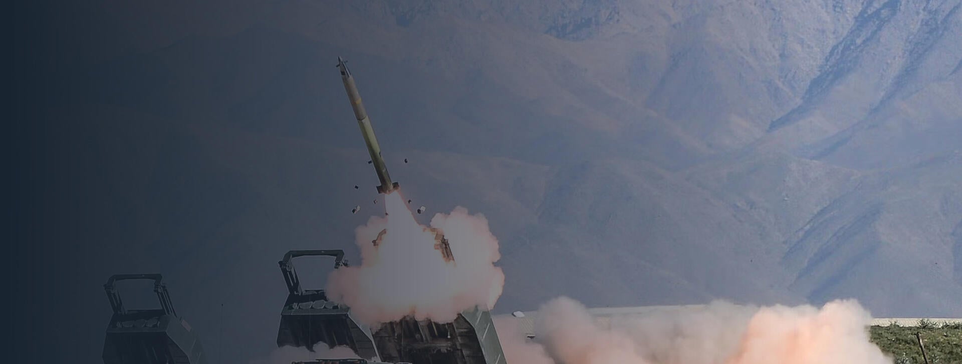 GMLRS rocket fires from HIMARS launcher with mountains in background