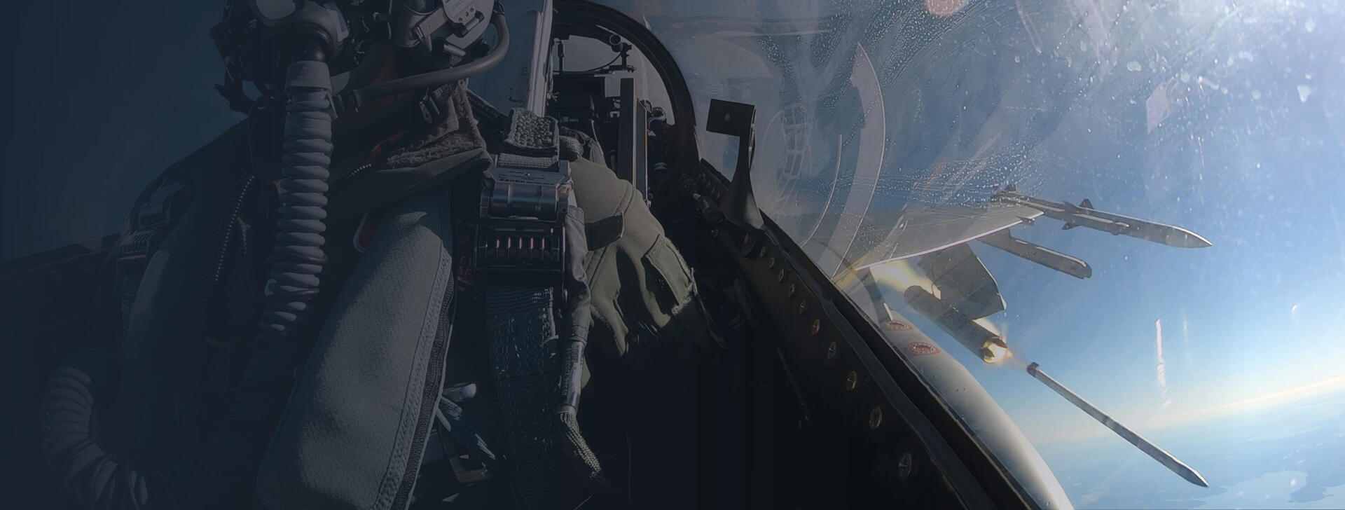 Pilot in cockpit with missiles firing in sky background