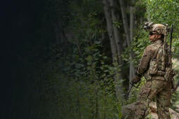 Soldier wearing communications equipment and night vision goggles in forest