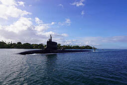 Submarine slices through water surface under a blue sky