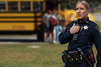 Sheriff using portable radio in front of school bus