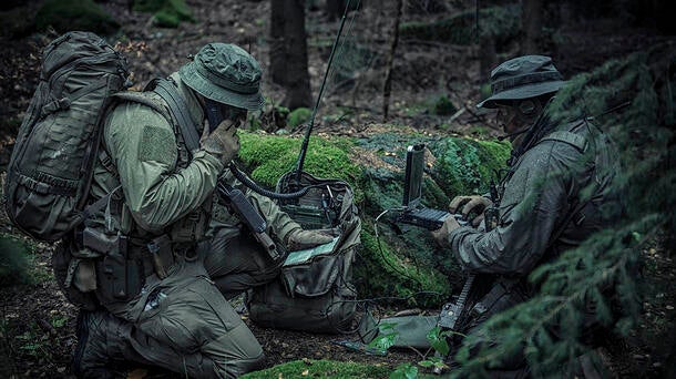 Soldiers using manpack radio in wooded area