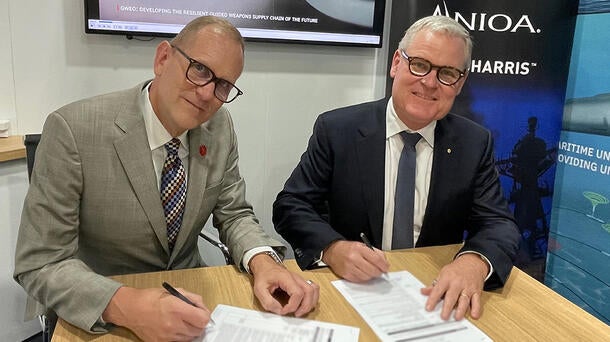 Two executives sign paperwork at a desk