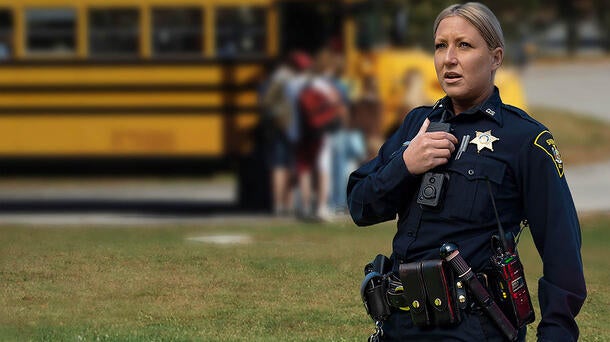 Sheriff using portable radio in front of school bus