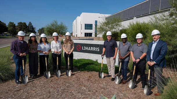 Employees stand in front of an L3Harris sign with shovels and hard hats