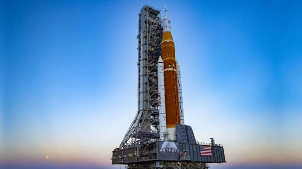 Down the transfer aisle from the Artemis II SLS core stage, an overhead crane hoists the left aft assembly, or bottom portion of the solid rocket boosters for the SLS Moon rocket inside the Vehicle Assembly Building at NASA’s Kennedy Space Center. Photo credit: NASA.