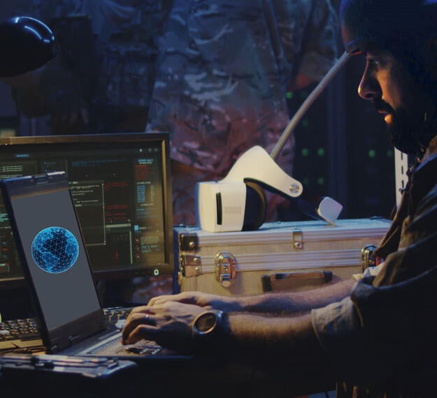 Multi-Domain Situational Awareness Concept image with soldier at laptop and soldiers in fatigues standing in background