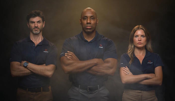 Three L3Harris employees stand with arms crossed