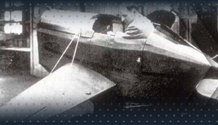 Black and white photograph of a man sitting in a small plane simulator