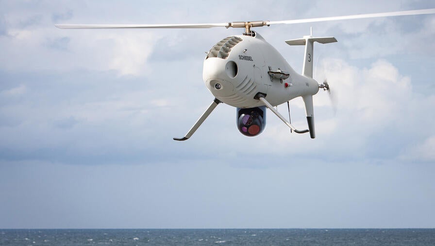 A Shiebel S100 unmanned autonomous vehicle hovers over the open sea.