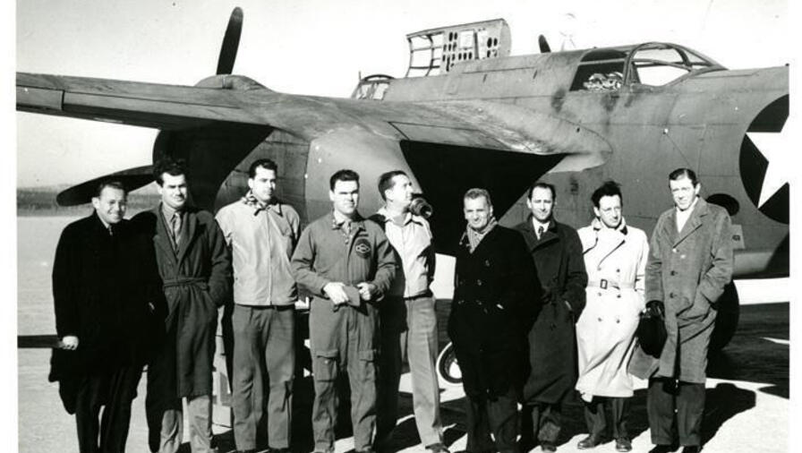 A black and white photo of a group of men in front of a plane