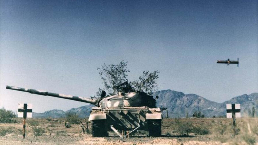 A missile flies above a tank in a field with mountains in the background