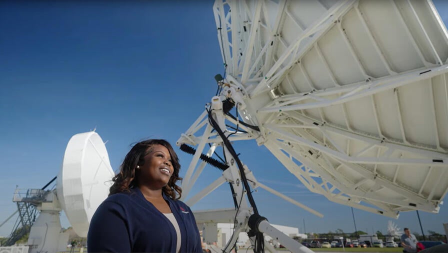 L3Harris employee stands in front of satellite technology