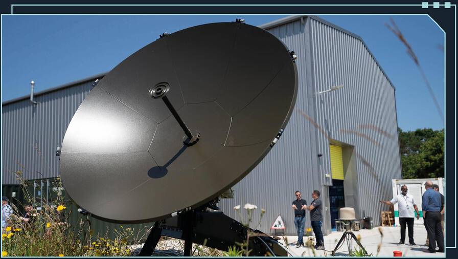 large sat comms dish positioned on grass outside a large warehouse-style building
