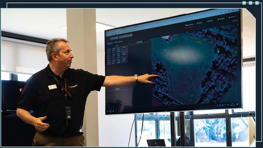 Engineer pointing to a large touchscreen showing a demo of 'Drone Guardian' software and capability