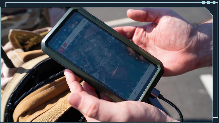 zoomed in shot of soldier's hands holding mobile device showing a map on the screen