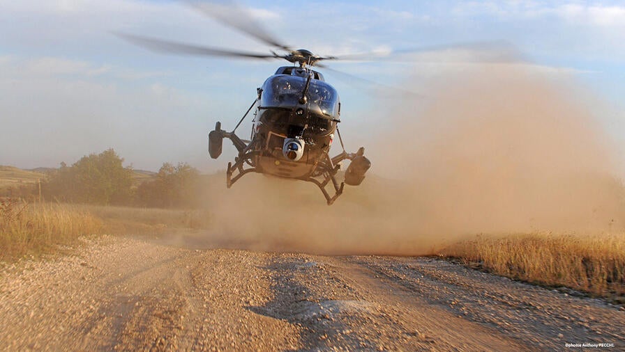 Airbus H145M landing on a dirt road with bellows of dust around it.