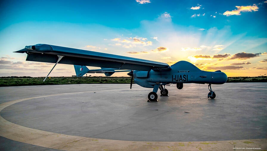 As sunset approaches, a Leonardo FALCO UAV sits on the tarmac, backlit by the golden sun.